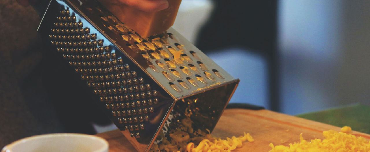 cheese being grated on a metal cheese grater onto wooden cutting board