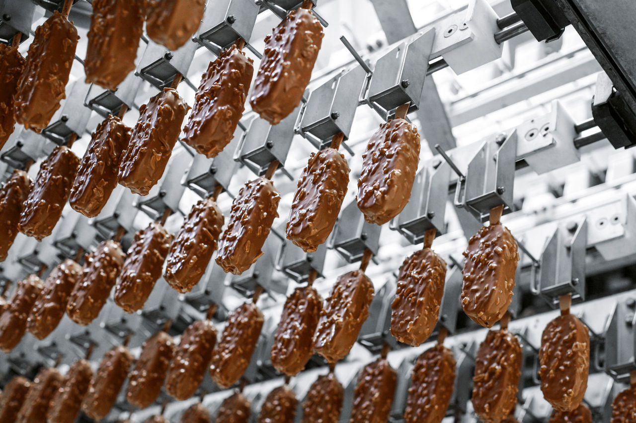 Rows of ice cream hanging from sticks on conveyor