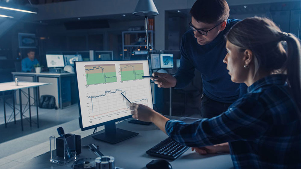 Engineer Working on Desktop Computer, Screen Showing CAD Software with Technical Blueprints, Her Male Project Manager Explains Job Specifics. Industrial Design Engineering Facility Office